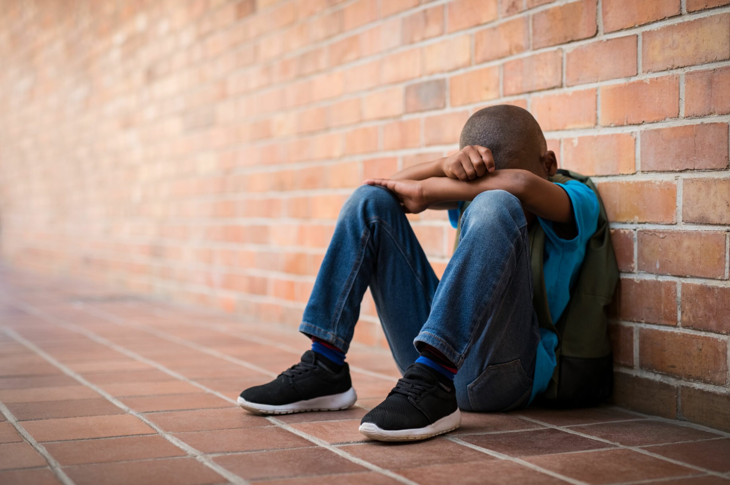 Child Sitting Against School Wall